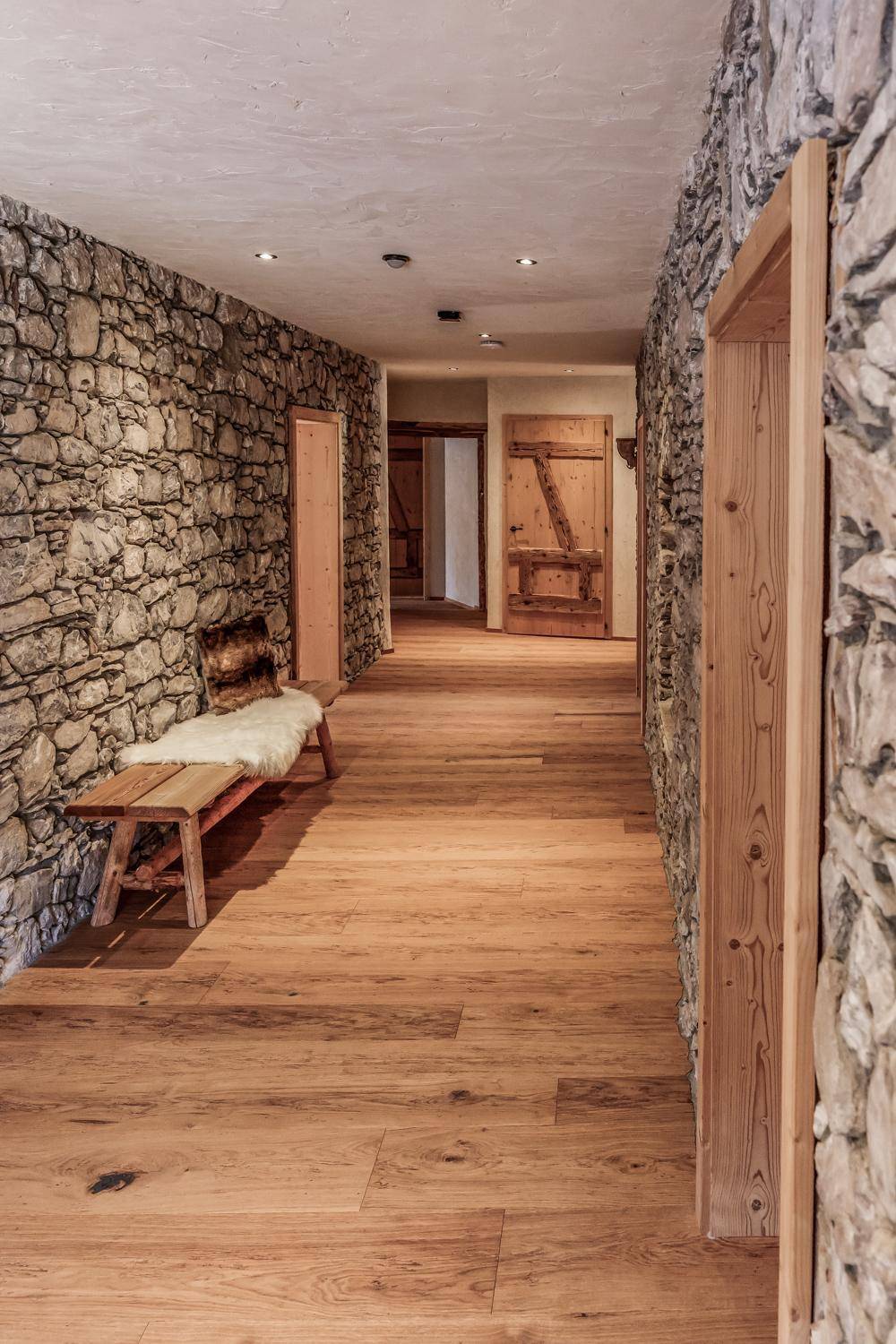 Rustikaler Flur mit Natursteinwänden und Holzboden, der zu weiteren Räumen führt.