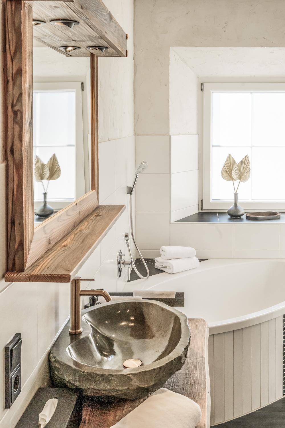 Elegantes Badezimmer mit Steinwaschbecken, Holzdetails und einer einladenden Eckbadewanne.