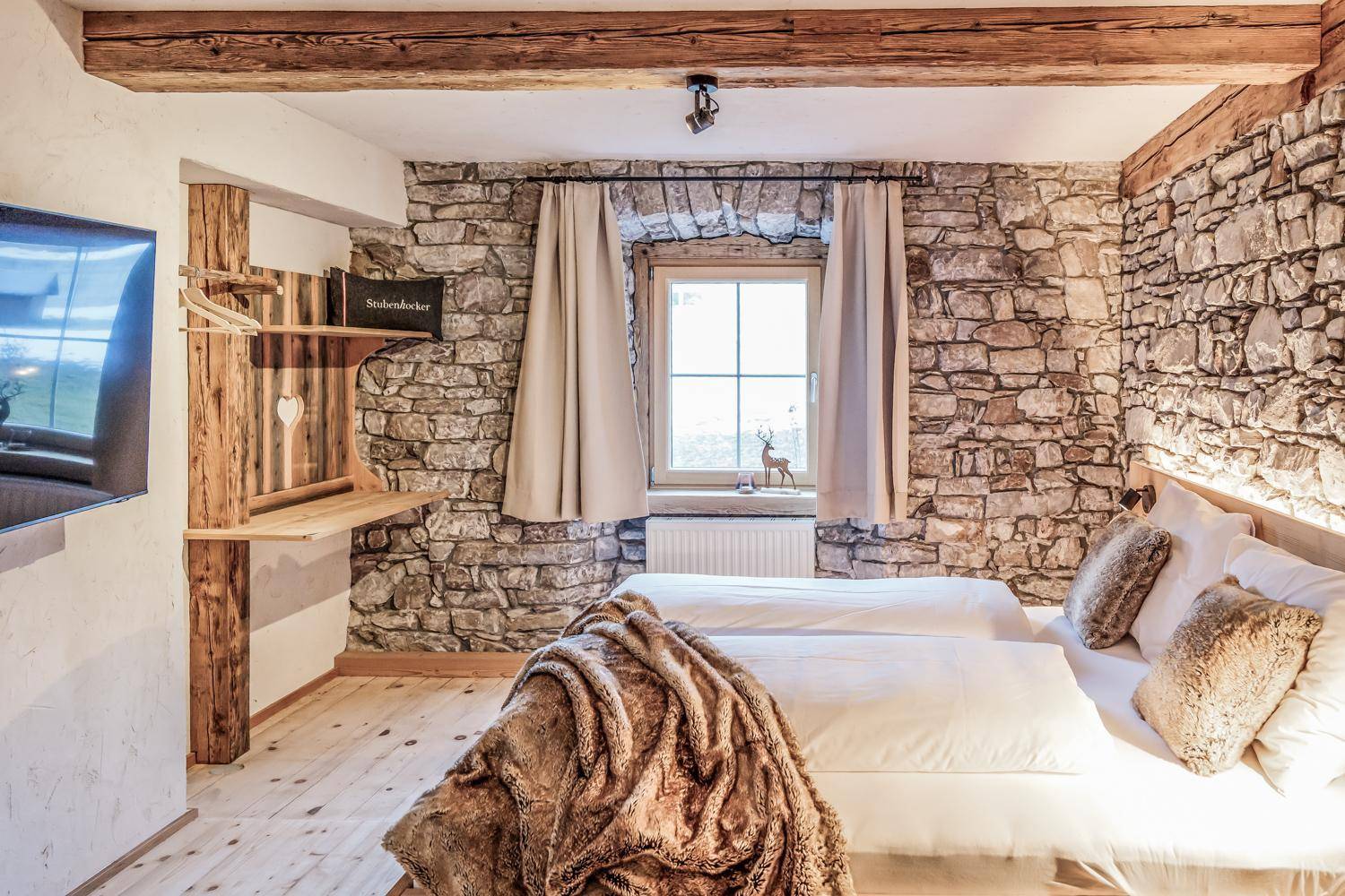 Schlafzimmer mit rustikalen Steinwänden, zwei Einzelbetten und einem praktischen Holzschreibtisch.