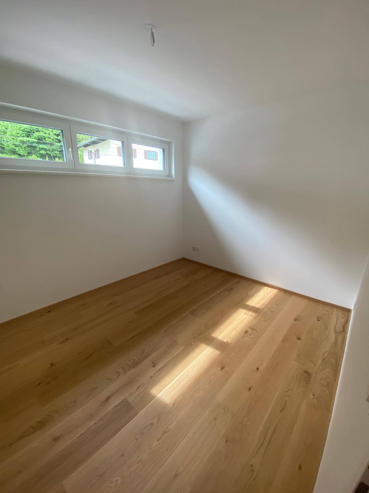 Helles Zimmer mit Holzboden und Fenster, das viel Tageslicht hereinlässt.
