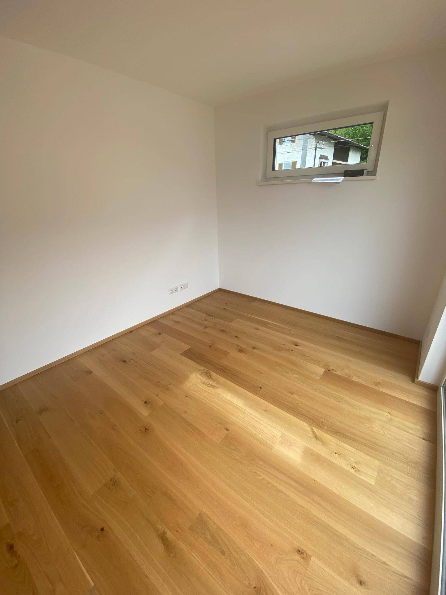 Leeres Zimmer mit hellem Holzboden und einem Fenster, bereit für individuelle Gestaltung.