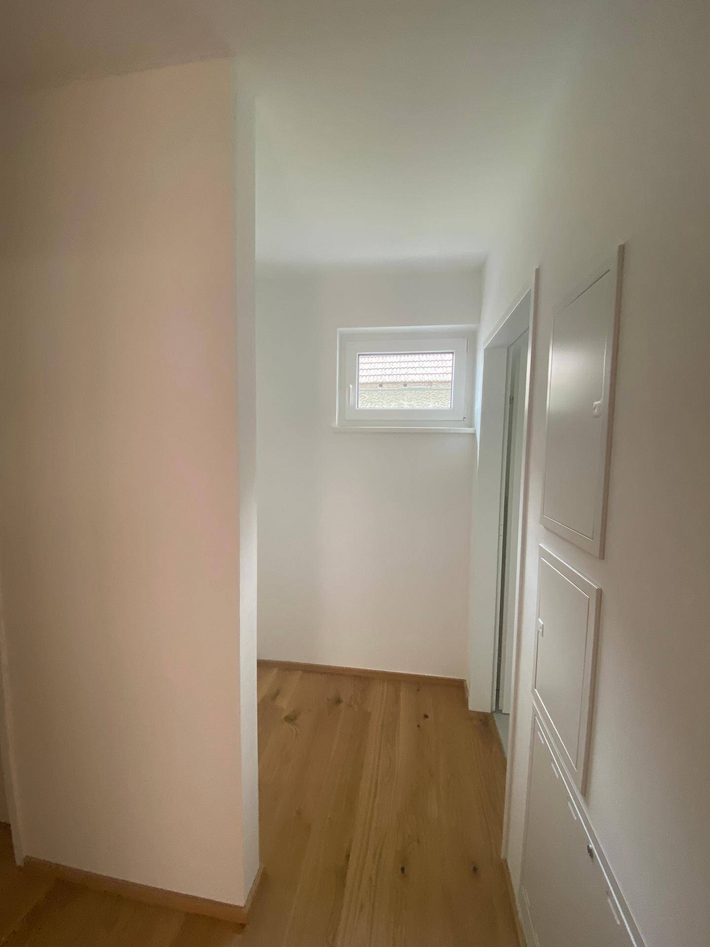 Heller Flur mit Holzboden und einem kleinen Fenster, das Tageslicht spendet.