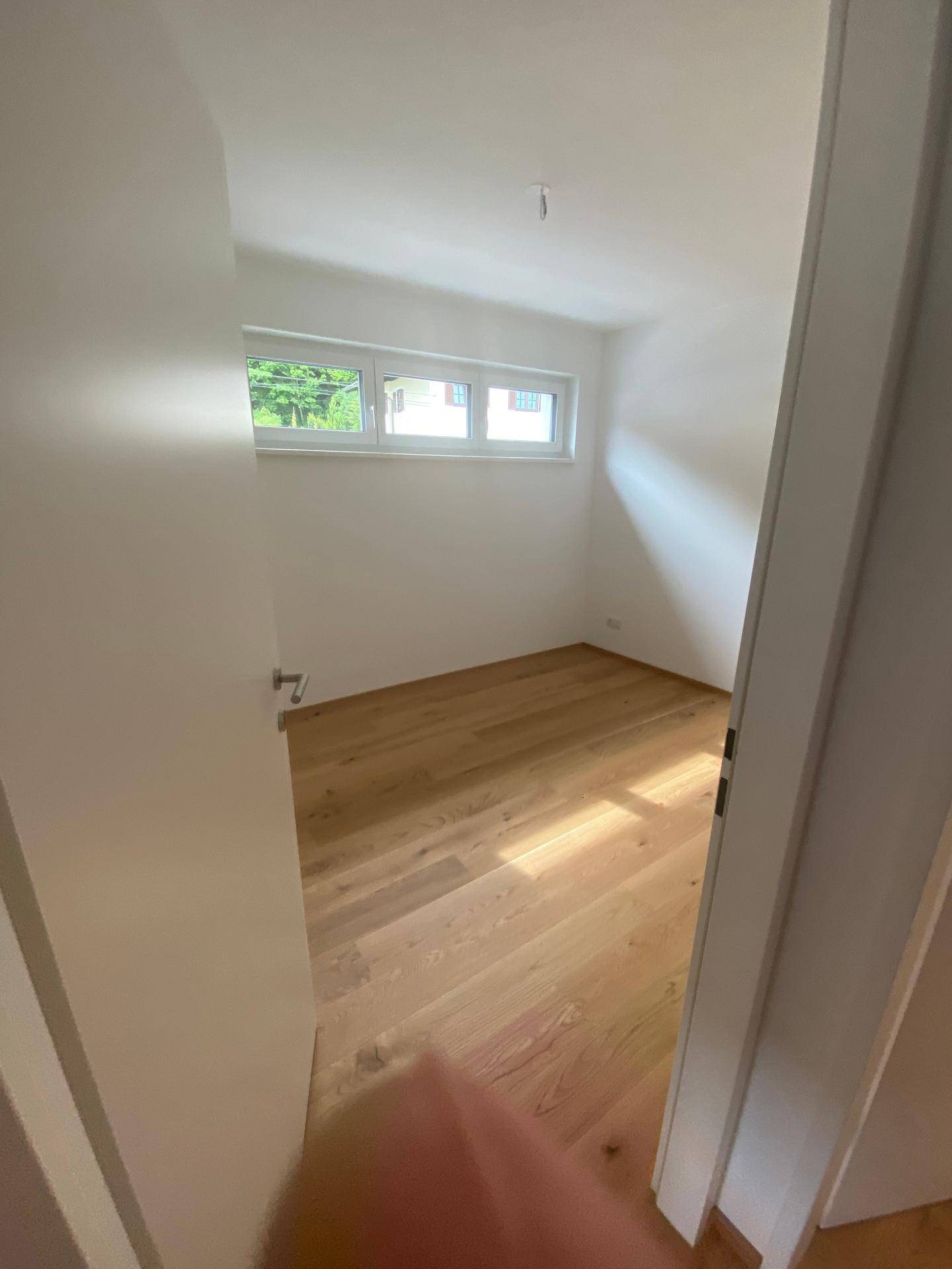 Leeres Zimmer mit Holzboden und weiß gestrichenen Wänden, bereit zur Einrichtung.