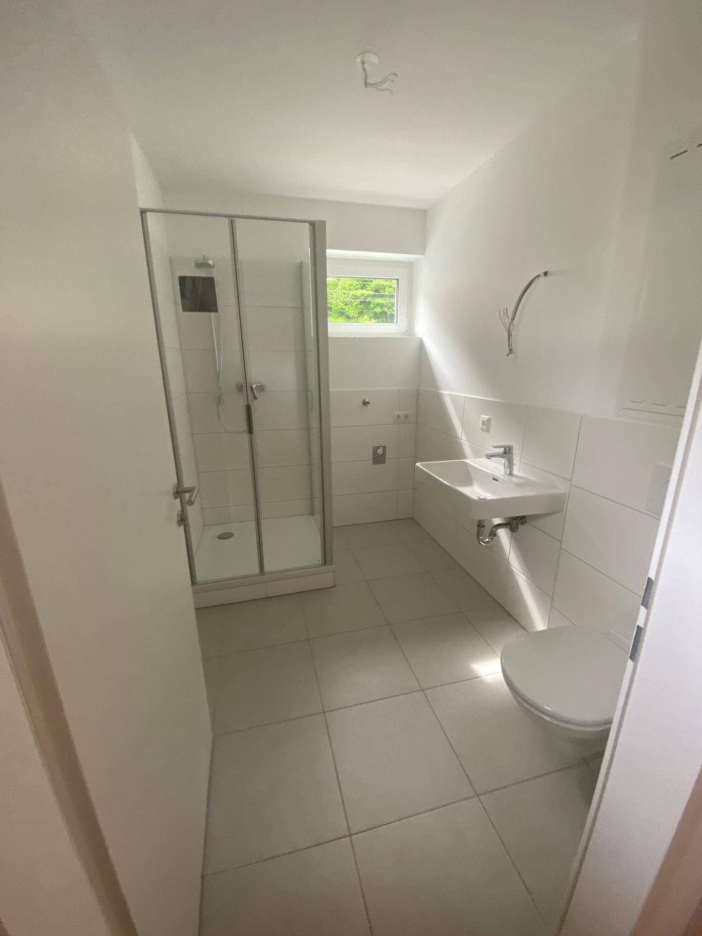 Modernes Badezimmer mit Dusche, WC, Waschbecken und Fenster für natürliche Belüftung.