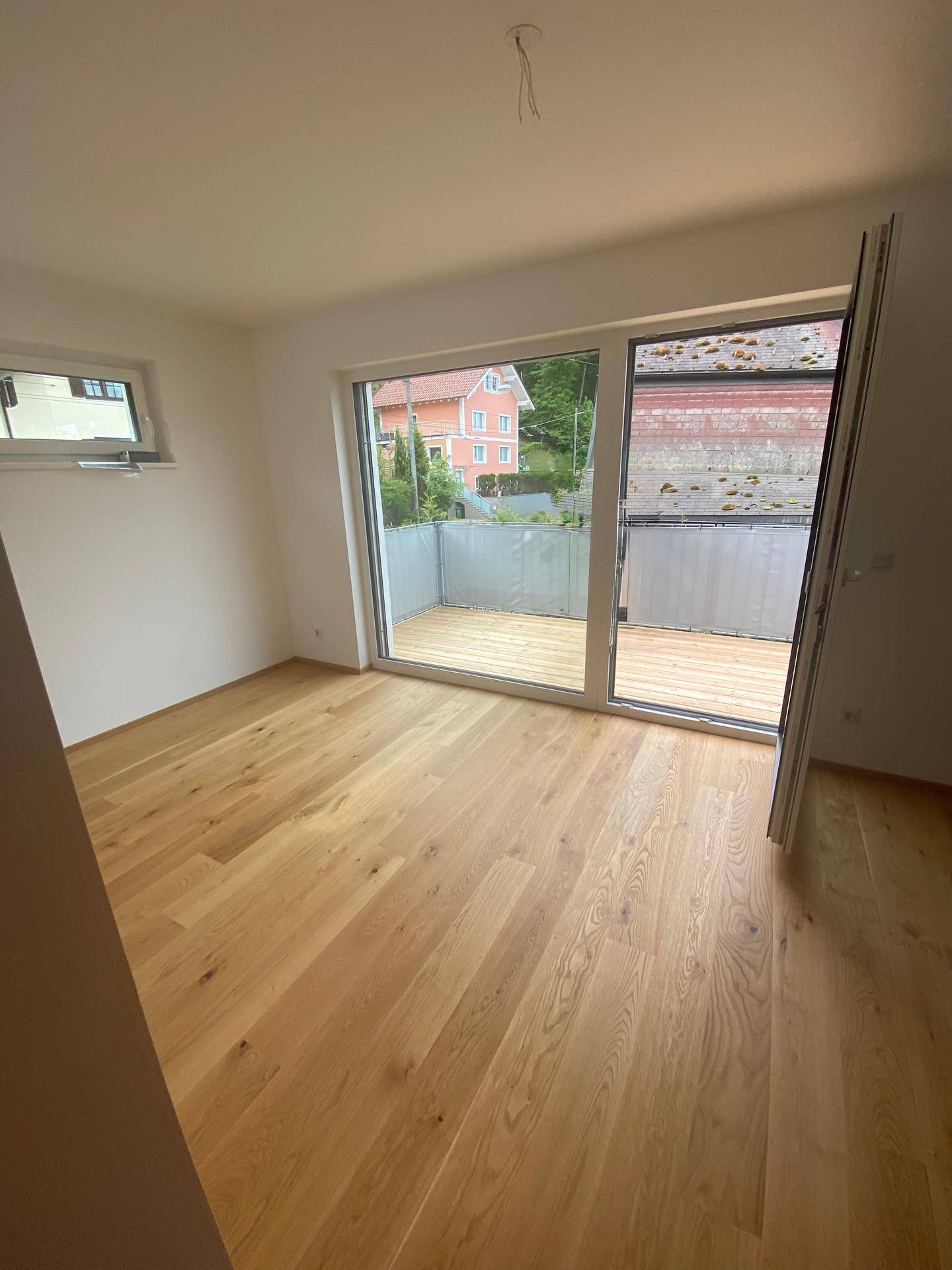 Helles Zimmer mit Holzboden und Zugang zu einem kleinen Balkon, ideal als Schlaf- oder Wohnbereich.