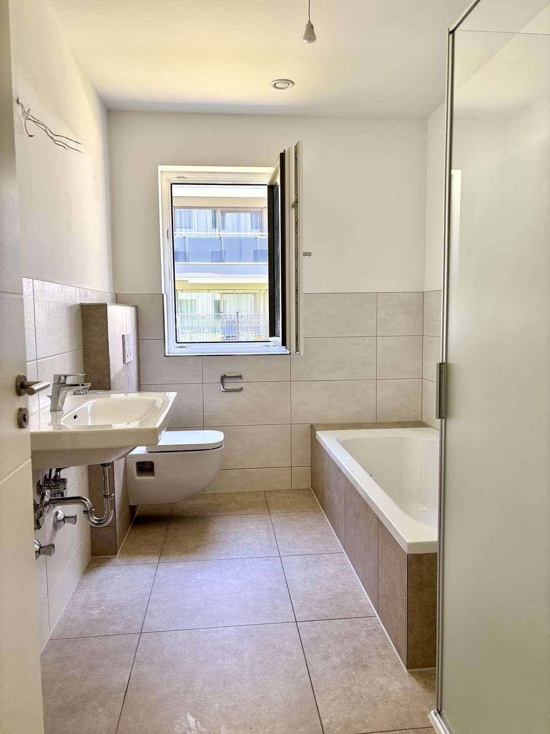 Modernes Badezimmer mit Badewanne, Dusche, WC, Waschbecken und einem Fenster für Tageslicht.