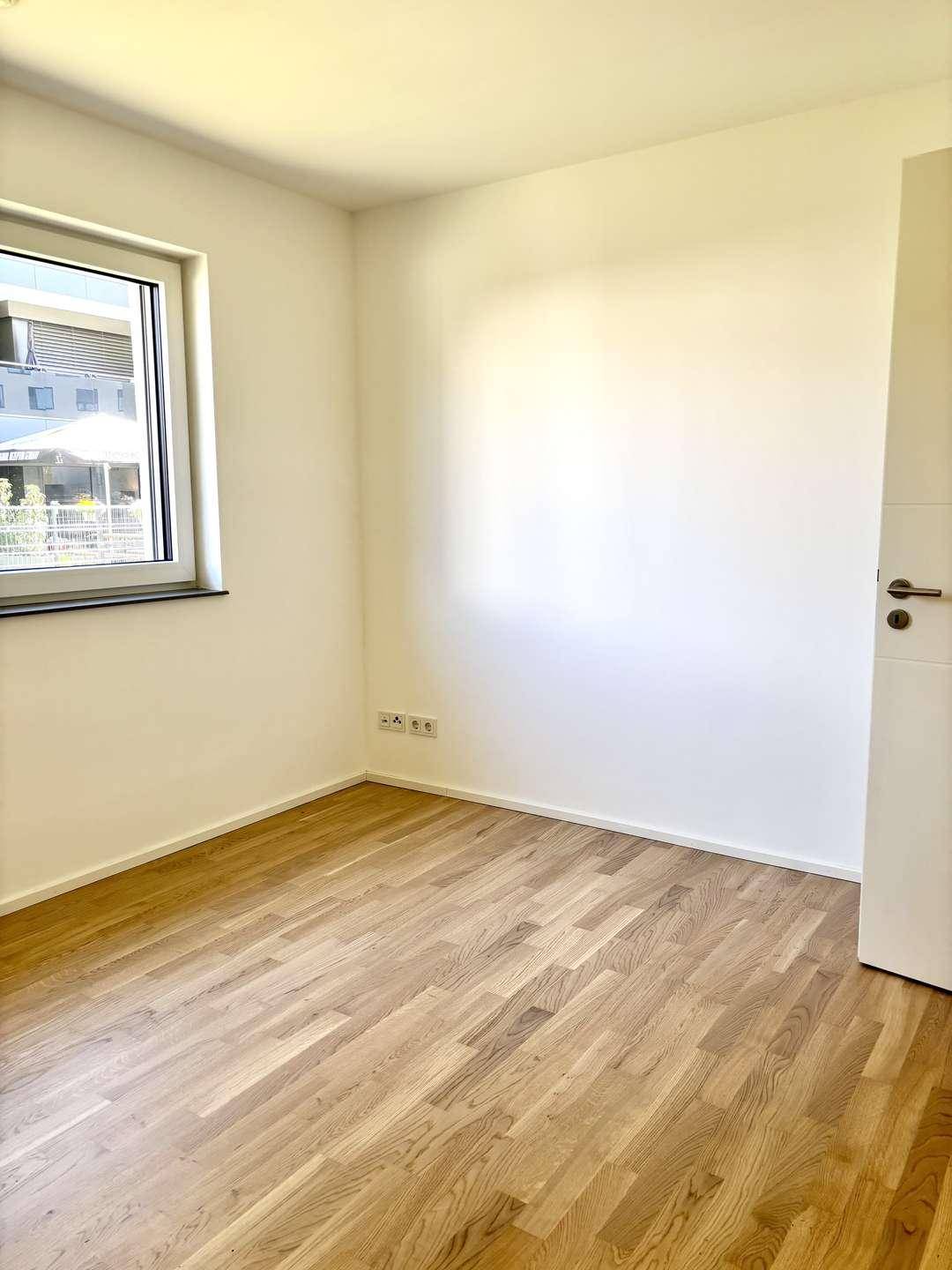 Geräumiges Schlafzimmer mit hellem Parkettboden und Fenster für viel Tageslicht.