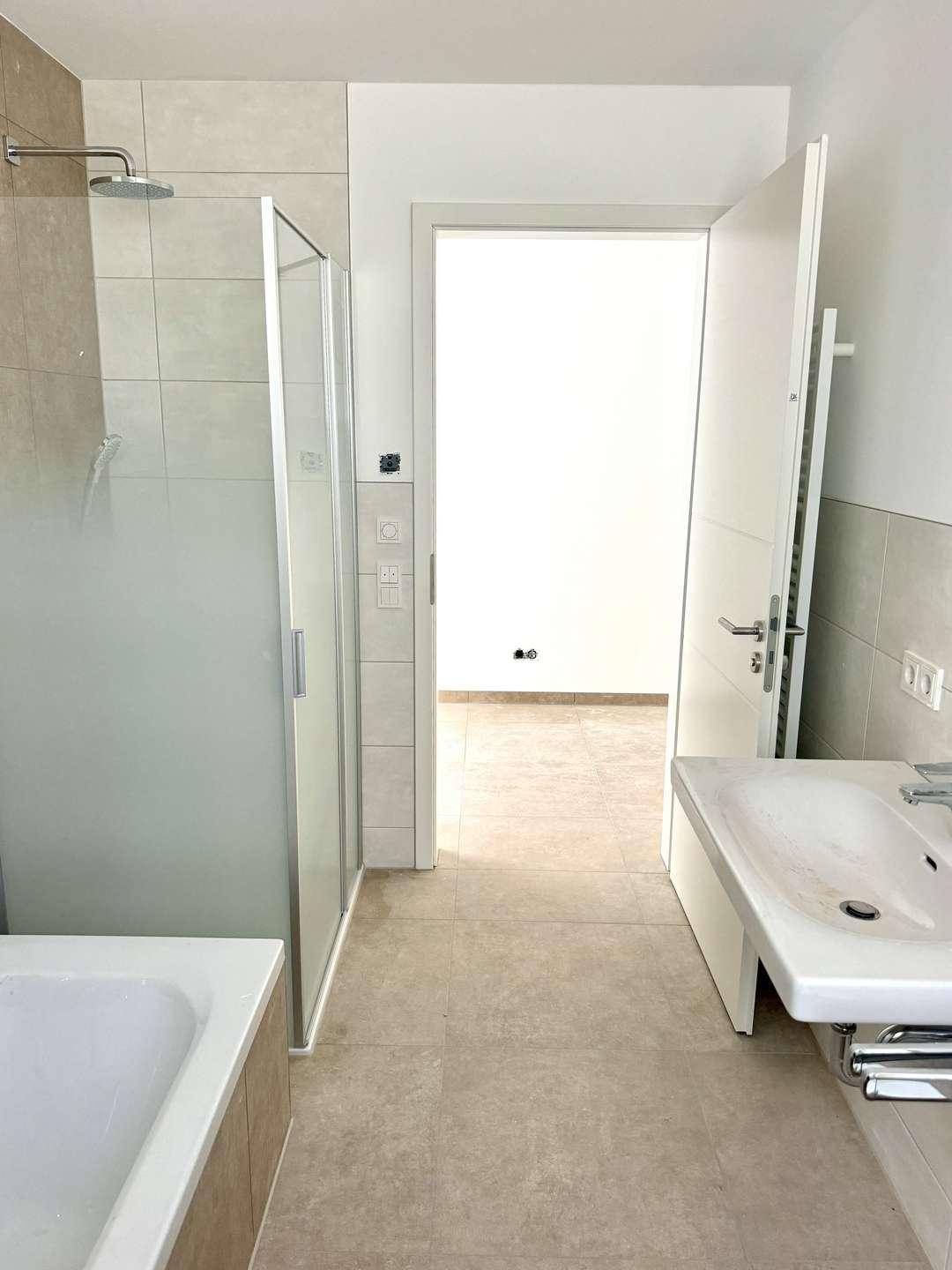 Geräumiges Badezimmer mit Duschkabine, Badewanne und Waschbecken, hell gefliest.