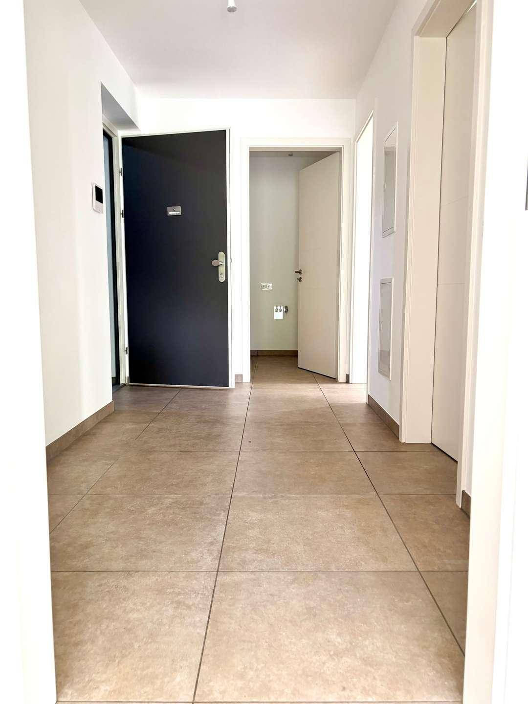 Eingangsbereich mit modernen Fliesen, der zu verschiedenen Zimmern der Wohnung führt.