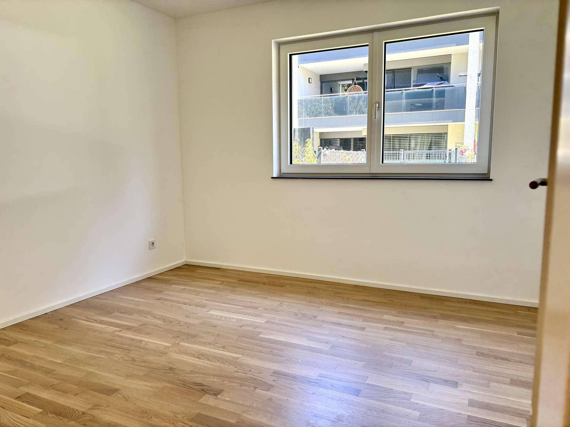 Helles Schlafzimmer mit Parkettboden und Fenster, das einen Blick auf die Umgebung bietet.