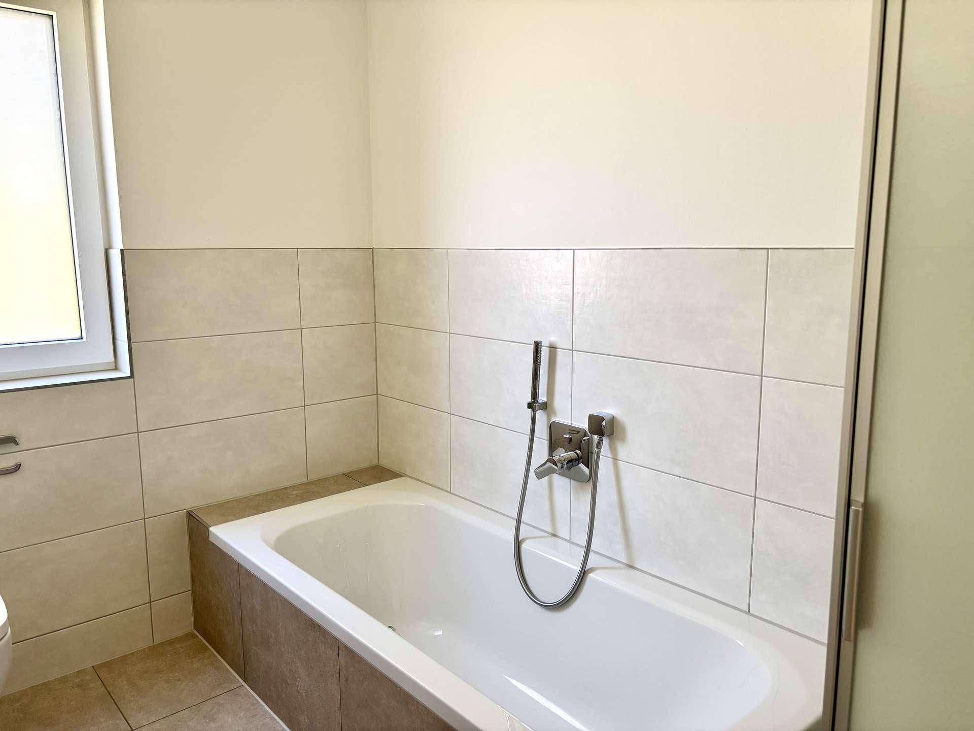 Detailansicht der Badewanne im modernen Badezimmer mit hellen Fliesen.