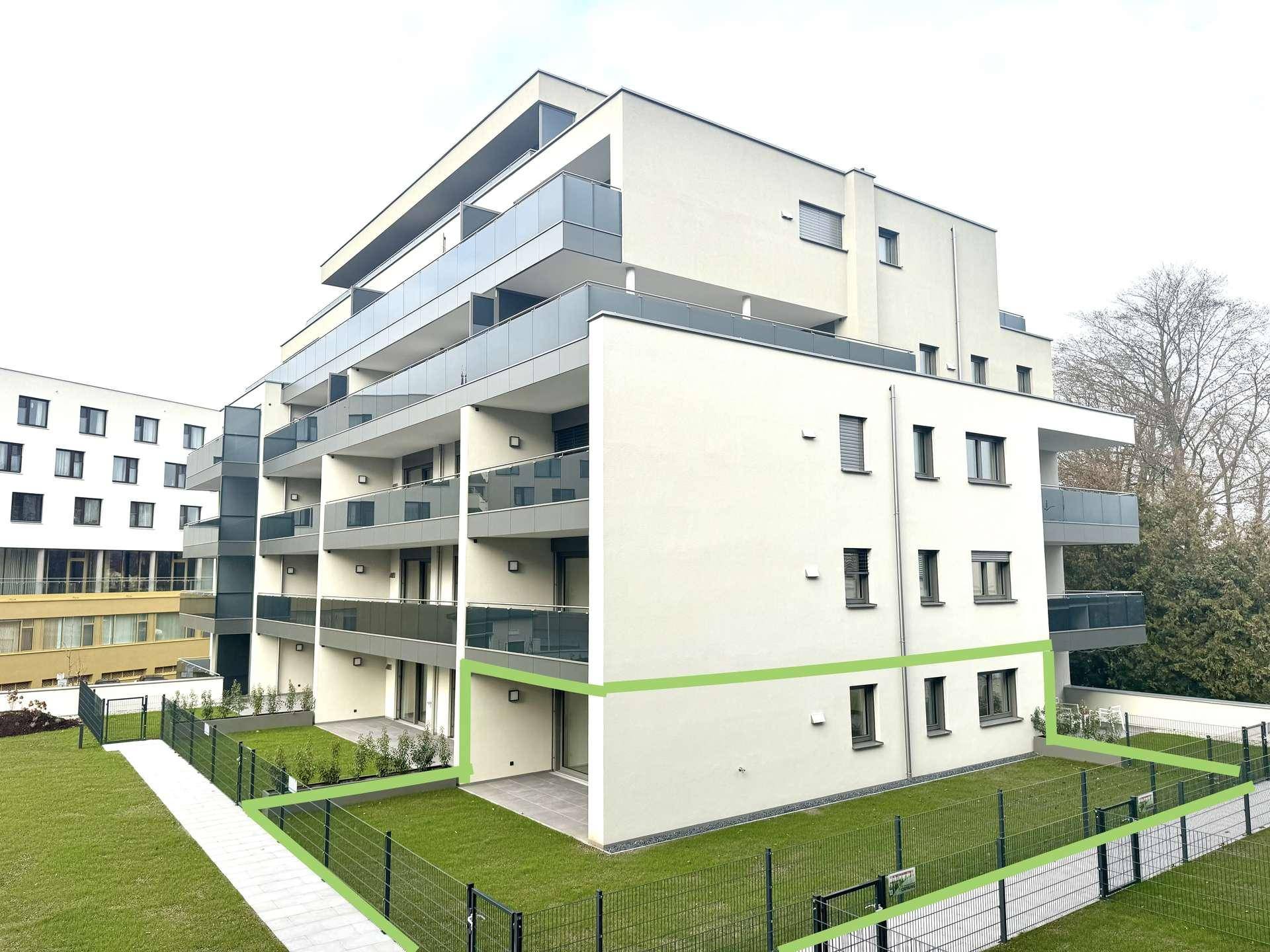 Moderne Wohnanlage mit Balkonen und einer Gartenfläche im Erdgeschoss, umgeben von Grün.
