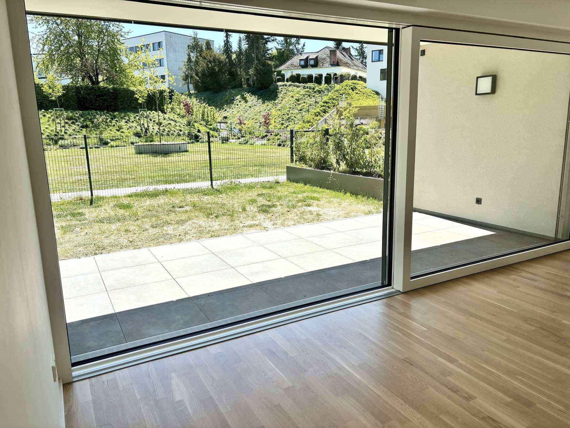 Große Glasfront mit Blick auf die geflieste Terrasse und den gepflegten Gartenbereich.