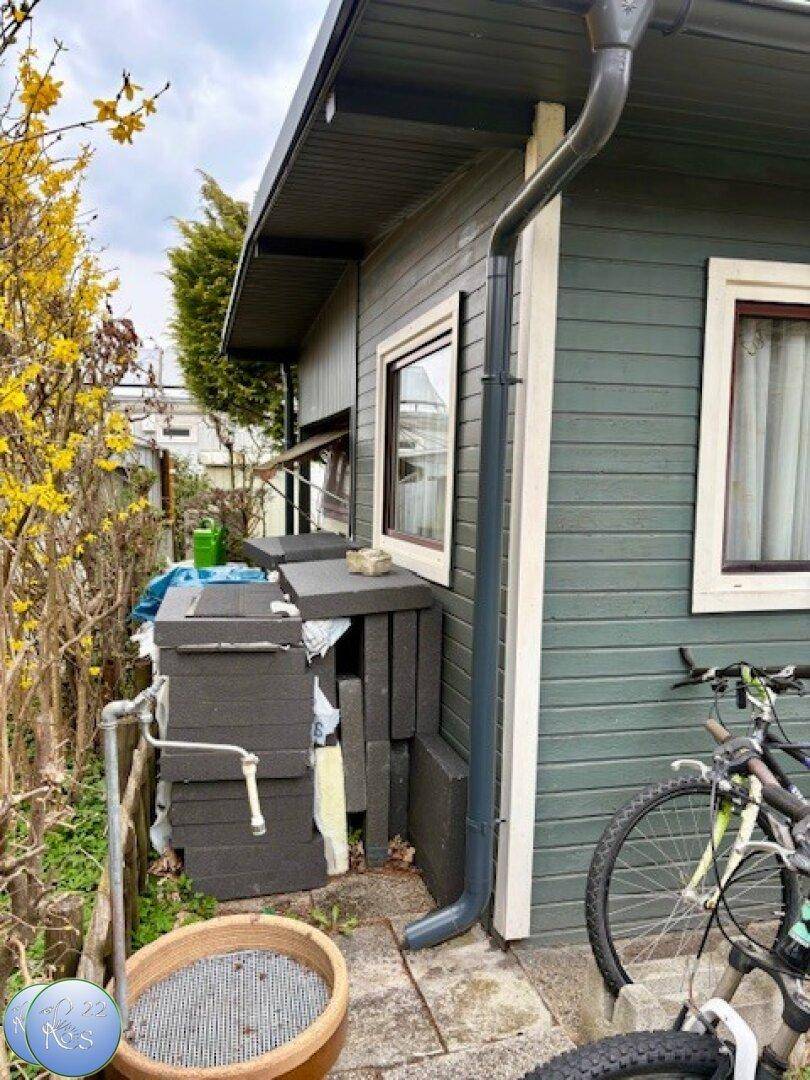 Seitenansicht des Ferienhauses mit Regenrinne, Außenwasserhahn und gelagertem Material.