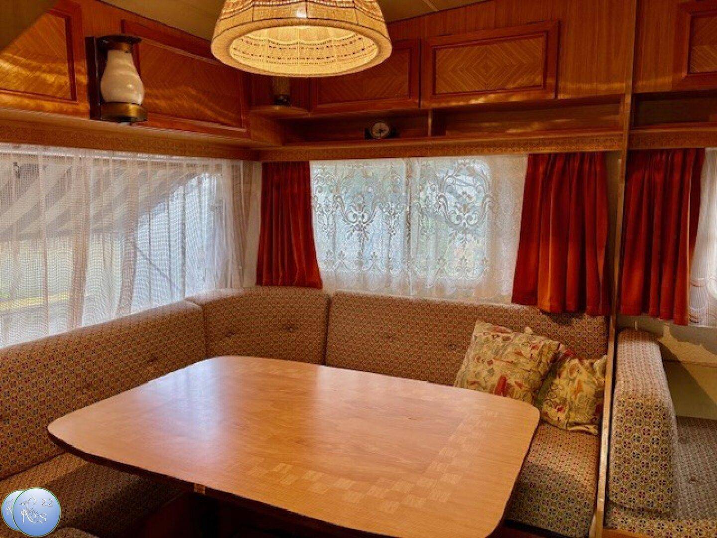 Kompakter Wohn- und Essbereich im Wohnwagen mit U-förmiger Sitzgruppe und Holztisch.