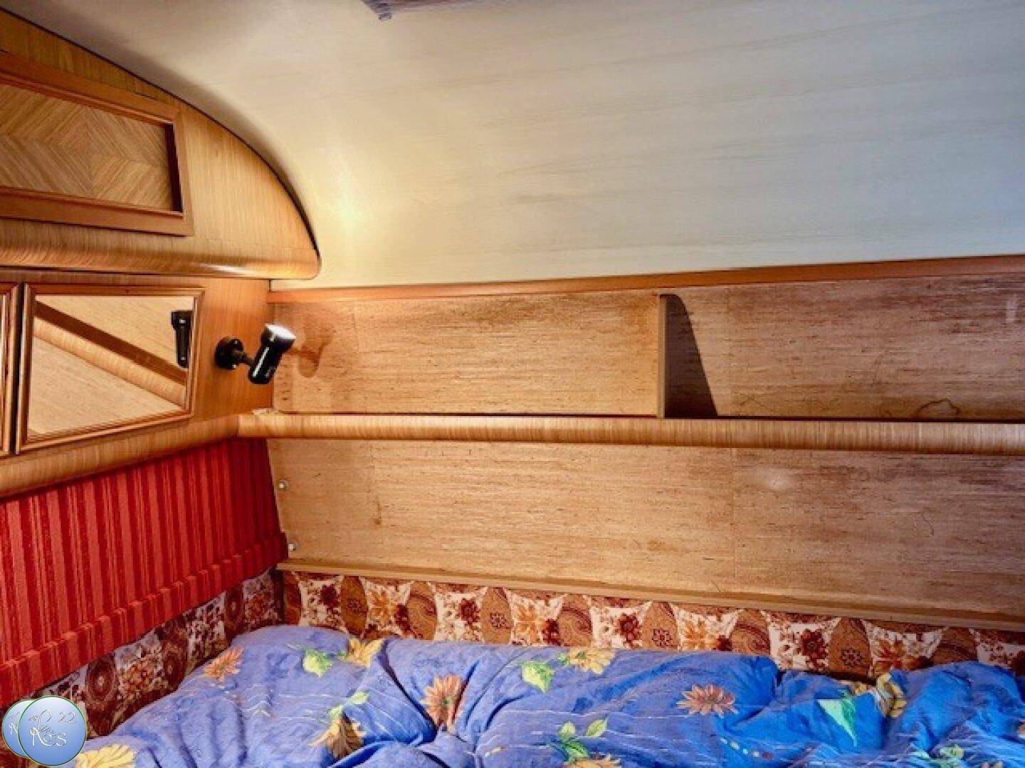 Schlafbereich im Wohnwagen mit Holzelementen, Ablagen und gemütlicher Beleuchtung.
