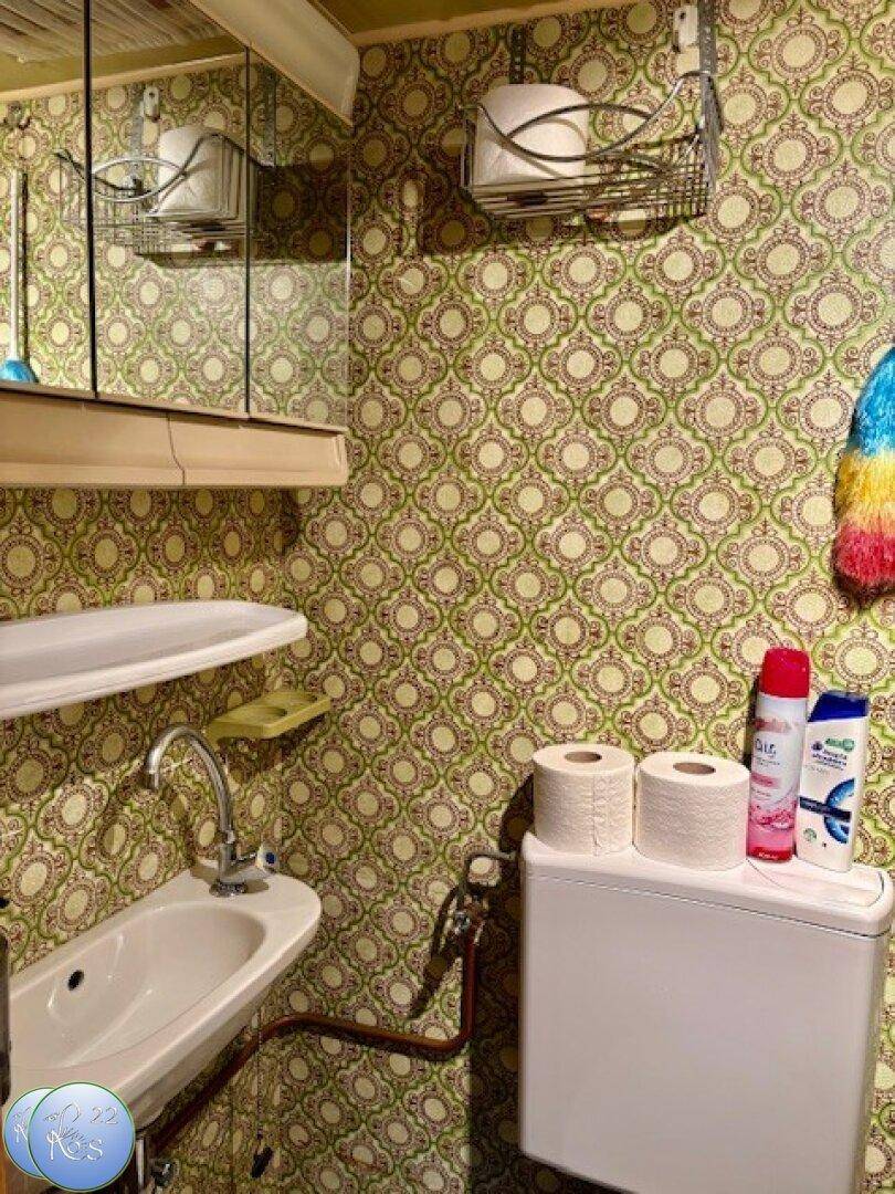 Kleines Badezimmer im 80er-Jahre-Stil mit gemusterter Tapete, Waschbecken und Toilette.