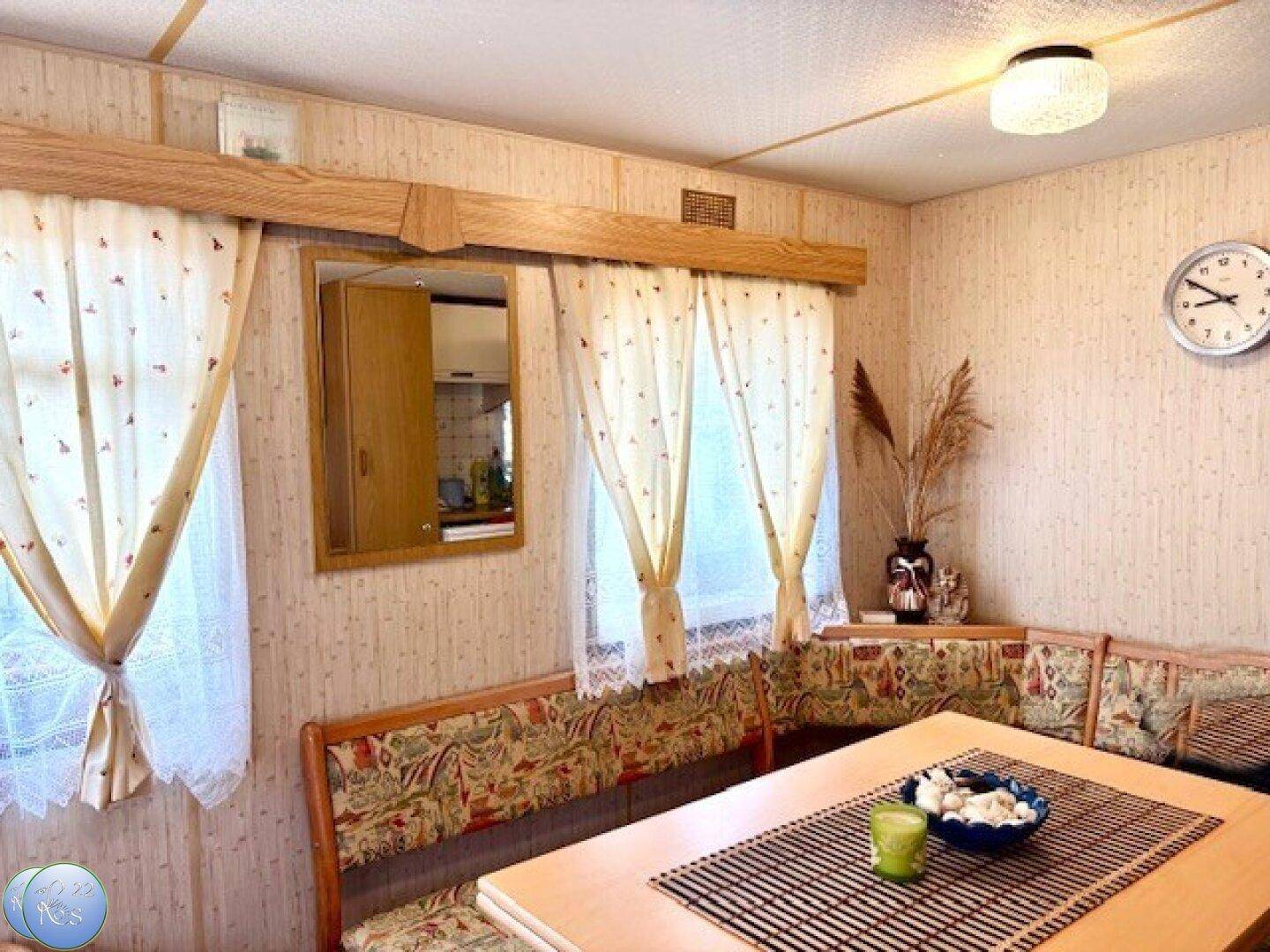 Gemütlicher Essbereich mit Eckbank, Holztisch und Fenstern mit Vorhängen.