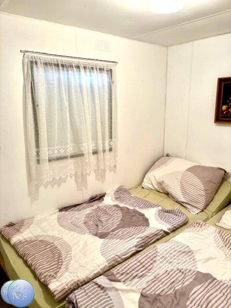 Schlafzimmer mit zwei Einzelbetten, schlichten Bettdecken und einem kleinen Fenster.