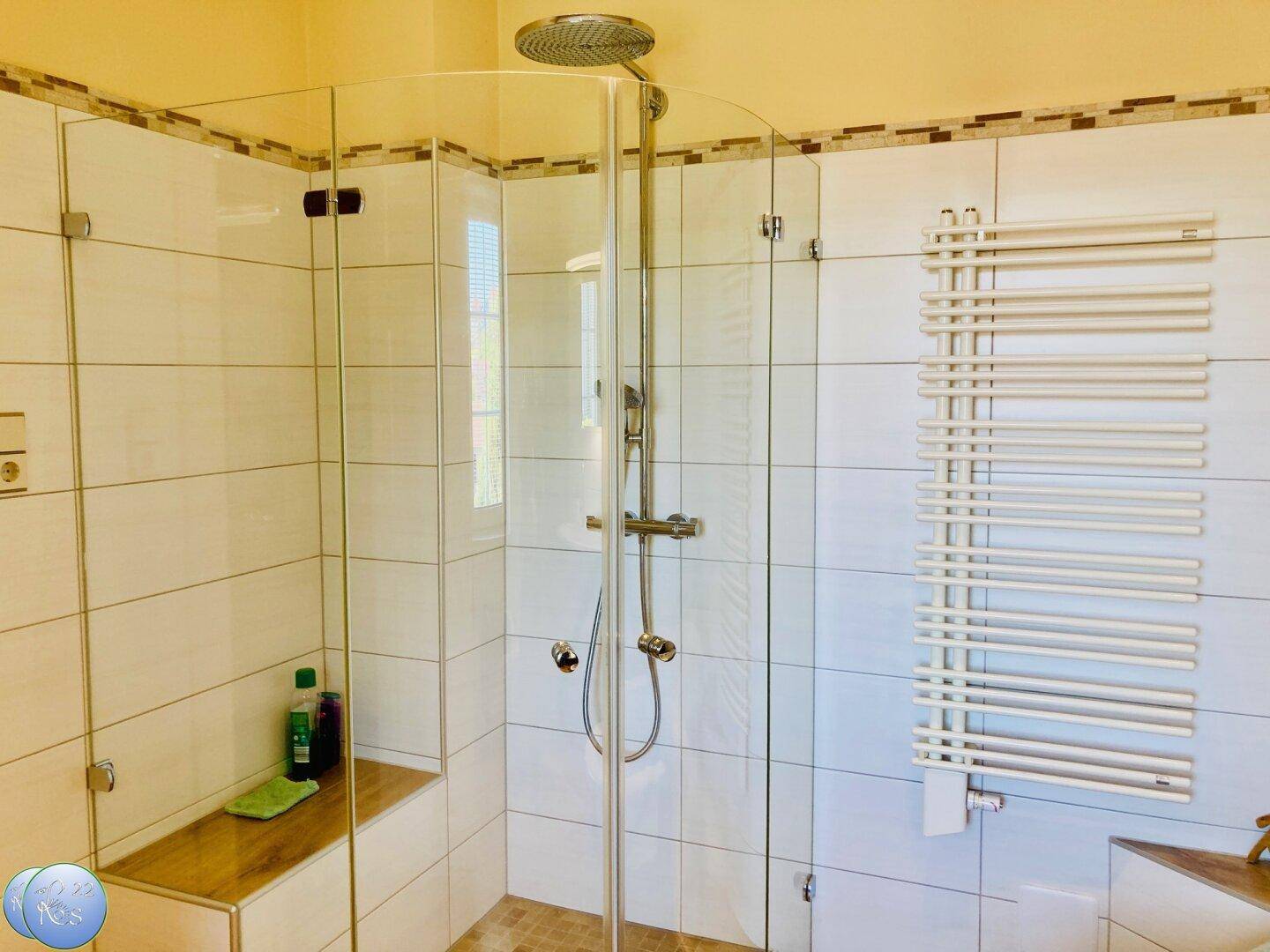 Modernes Badezimmer mit Eckdusche, weißen Fliesen und beheiztem Handtuchhalter.
