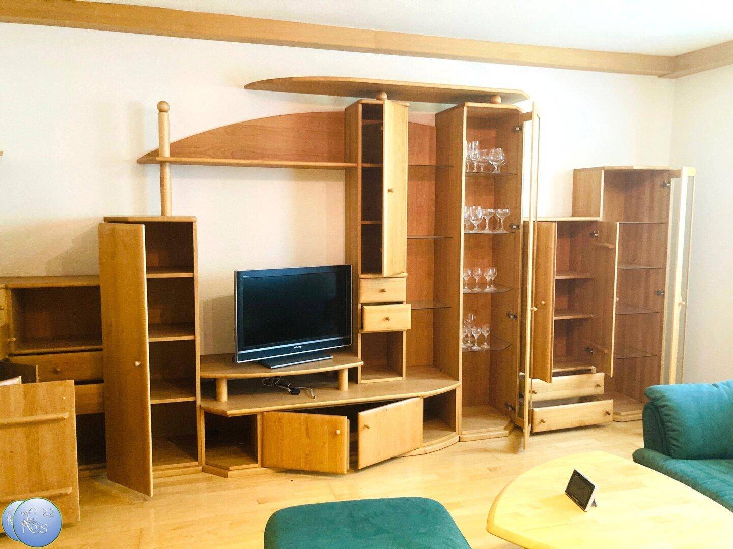 Geräumiges Wohnzimmer mit umfangreicher Holzschrankwand, Fernseher und gemütlicher Sitzecke.