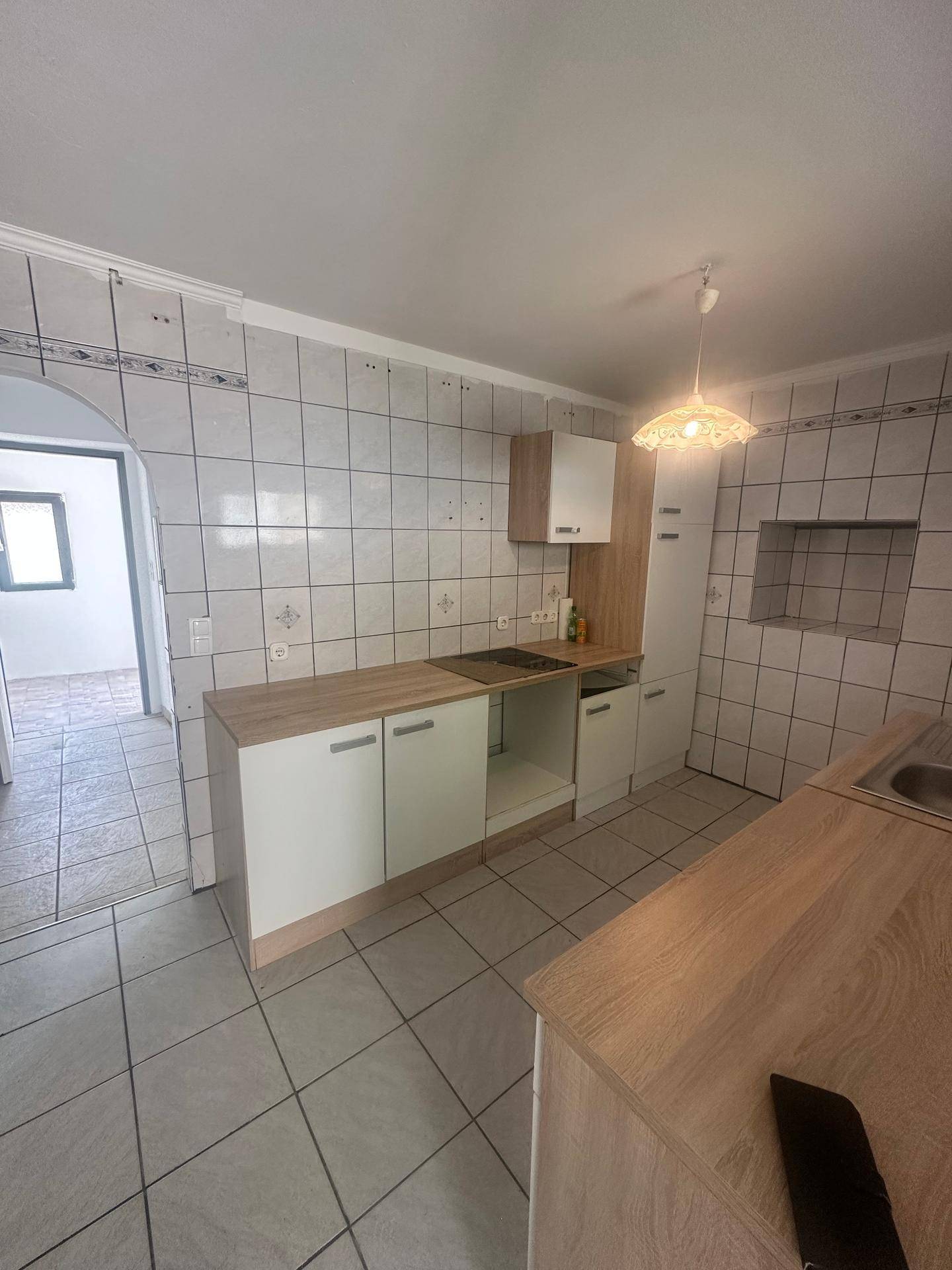 Küchenzeile mit hellen Holzfronten, gefliesten Wänden und einem Bereich für Kochgeräte.