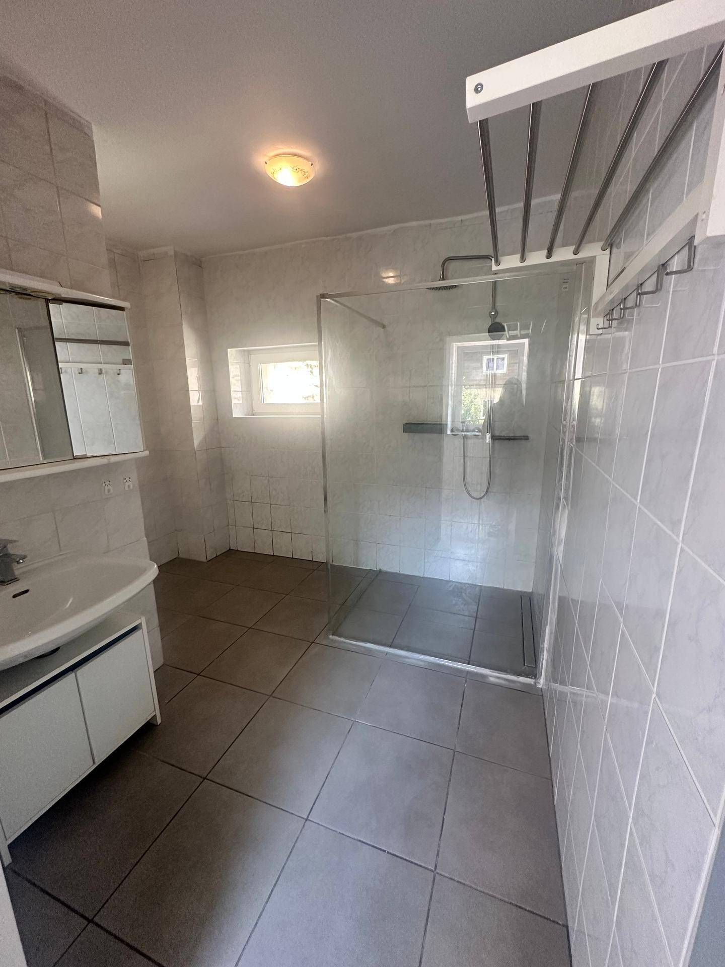 Modernes Badezimmer mit Fliesen, begehbarer Dusche, Waschbecken und einem kleinen Fenster.