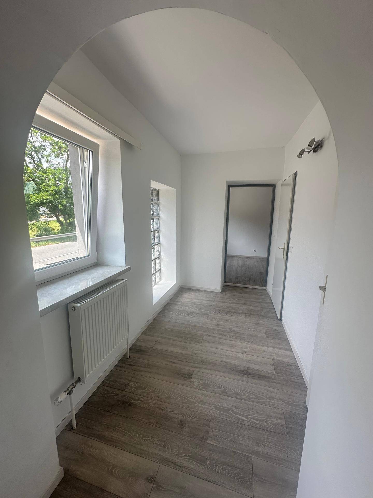 Lichtdurchfluteter Flur mit Laminatboden, großem Fenster und dekorativen Glasbausteinen.