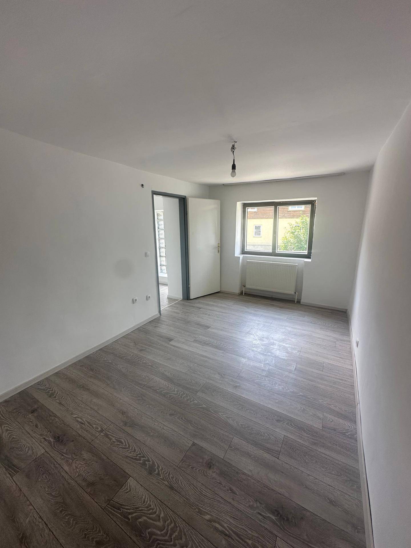 Leeres Schlafzimmer mit modernem Laminatboden, einem Fenster und einem Heizkörper.