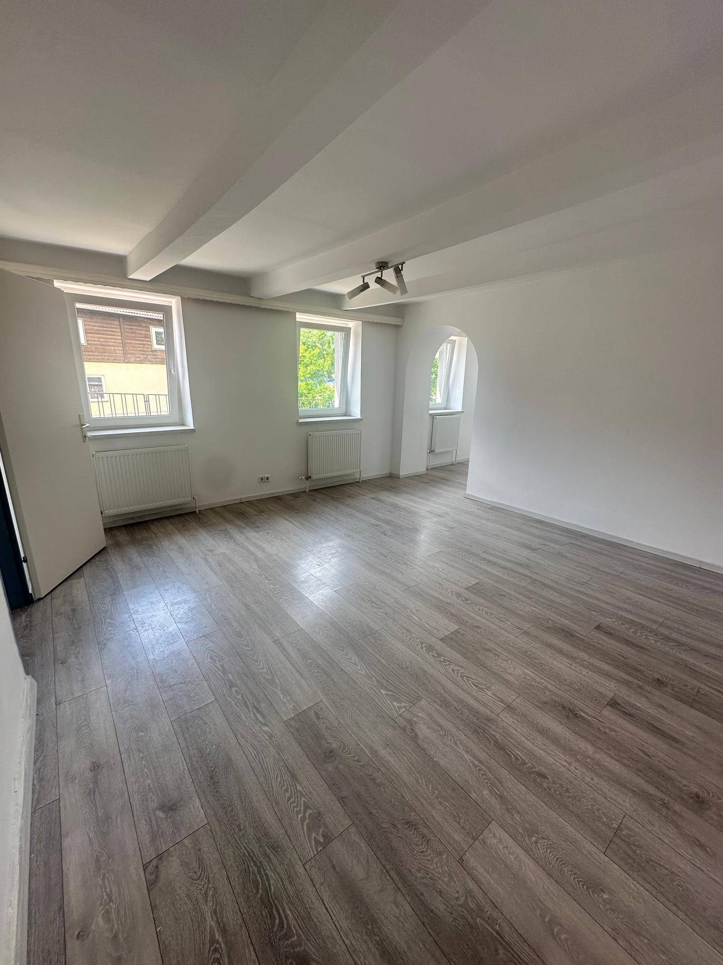 Heller Wohnraum mit Laminatboden, sichtbaren Deckenbalken und einem eleganten Bogendurchgang.