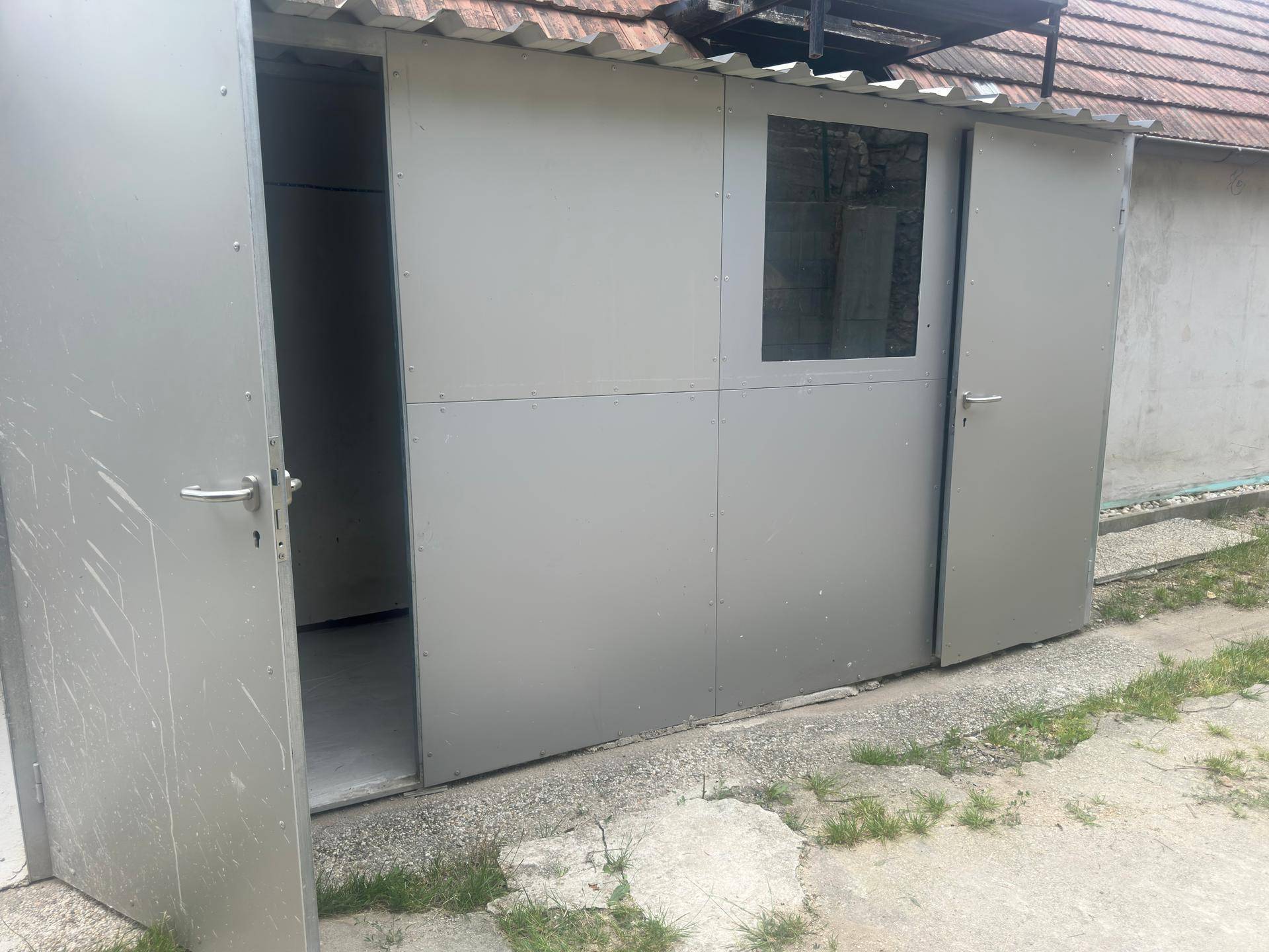 Kleines Gartenhaus oder Schuppen mit Metallverkleidung und zwei Türen im Außenbereich.