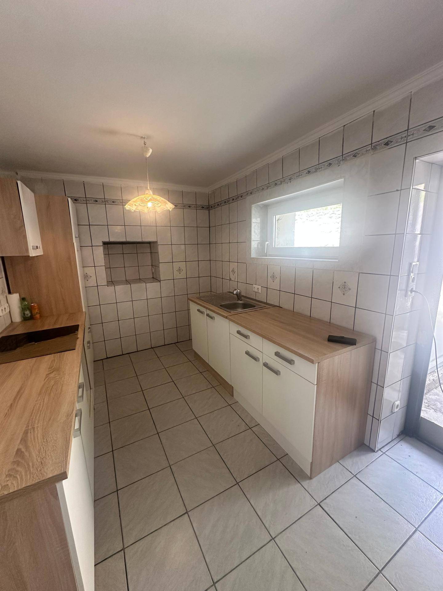 Einfache Küche mit gefliesten Wänden und Böden, Holz-Arbeitsplatten und einem Fenster.