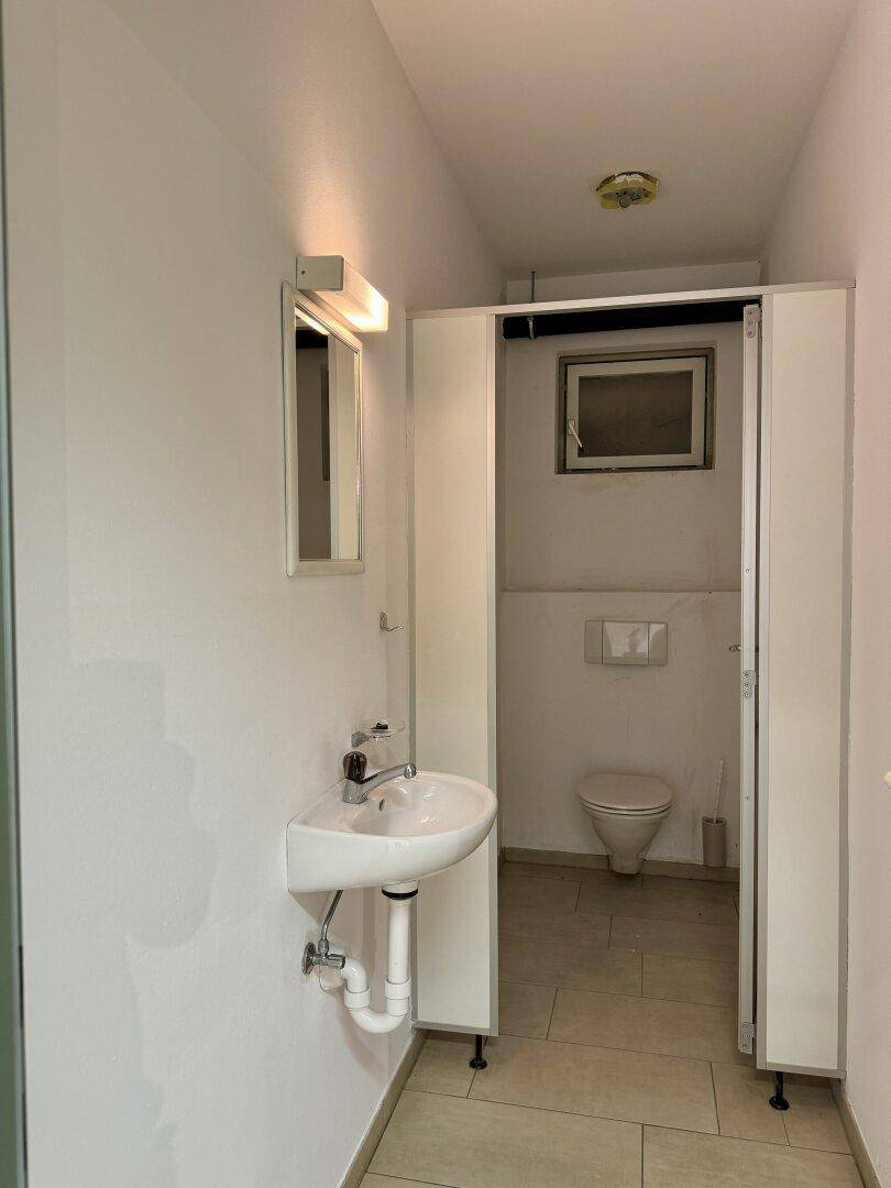 Sauberer Toilettenraum mit Waschbecken, Spiegel und einer Toilette, gut beleuchtet.