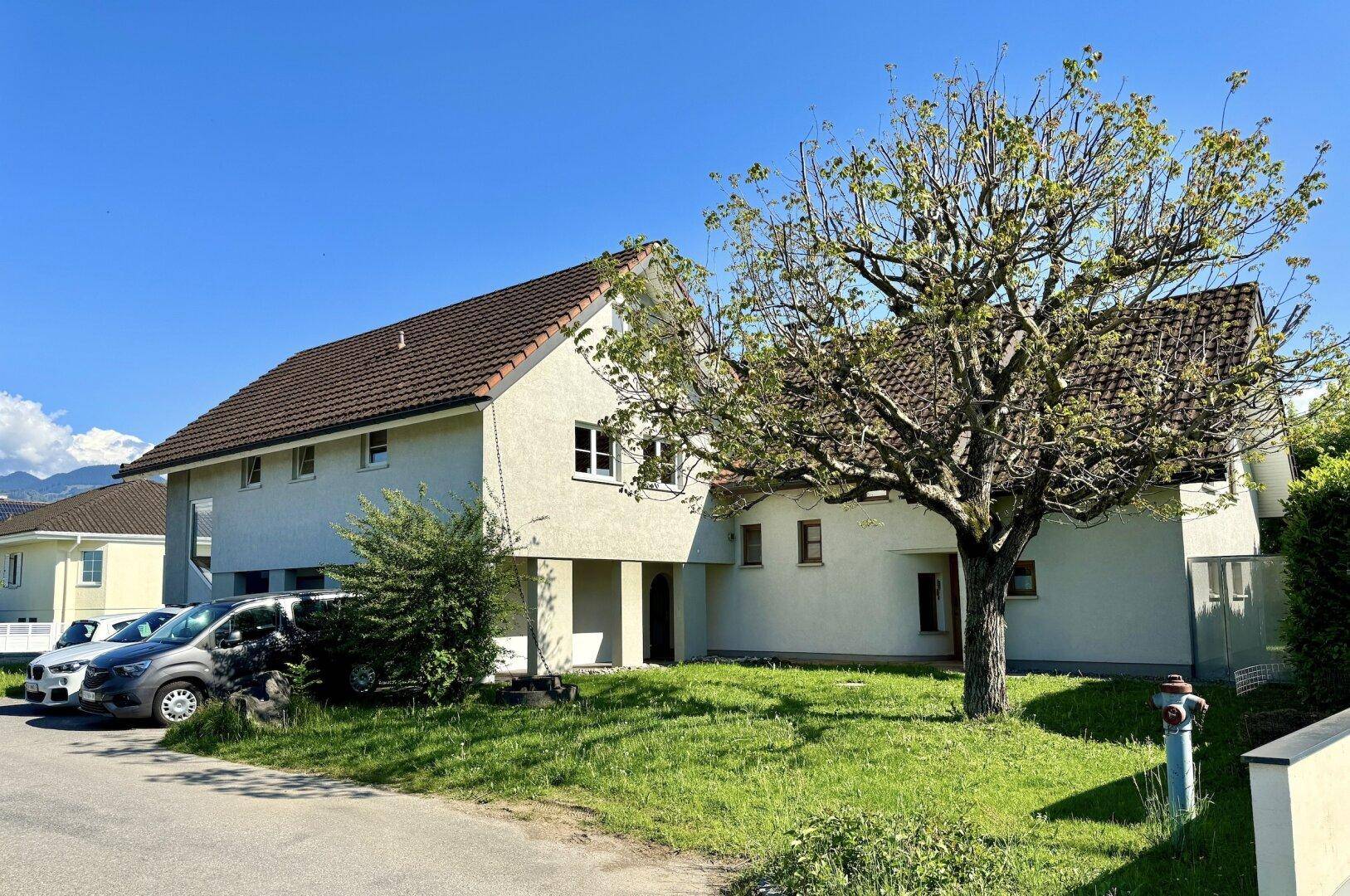 Seitenansicht des Hauses mit einem großen Baum im Vorgarten und Blick auf die umliegende Landschaft.
