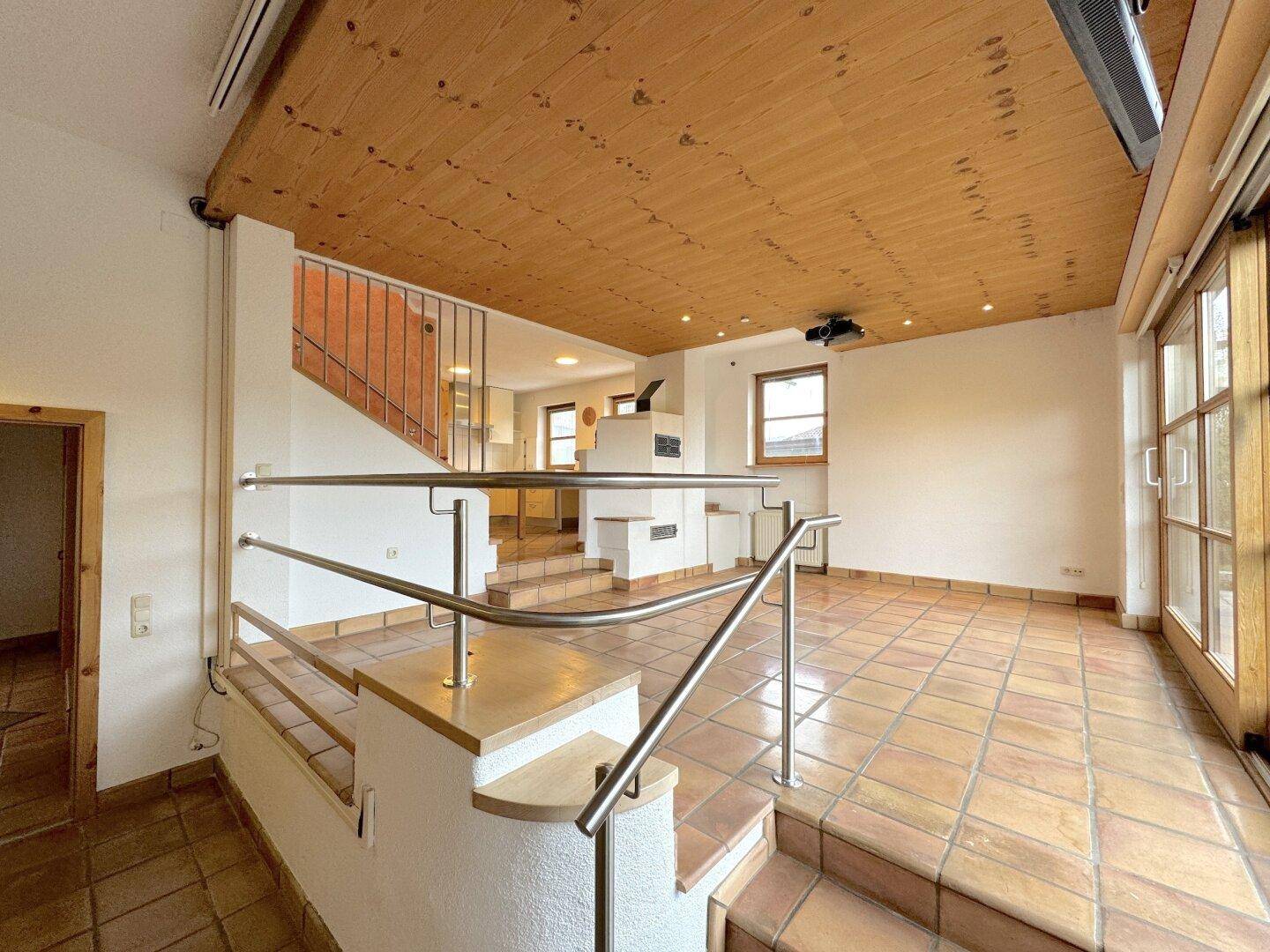 Geräumiges Wohnzimmer mit rustikalem Kachelofen, Holzdecke und Zugang zum Gartenbereich.