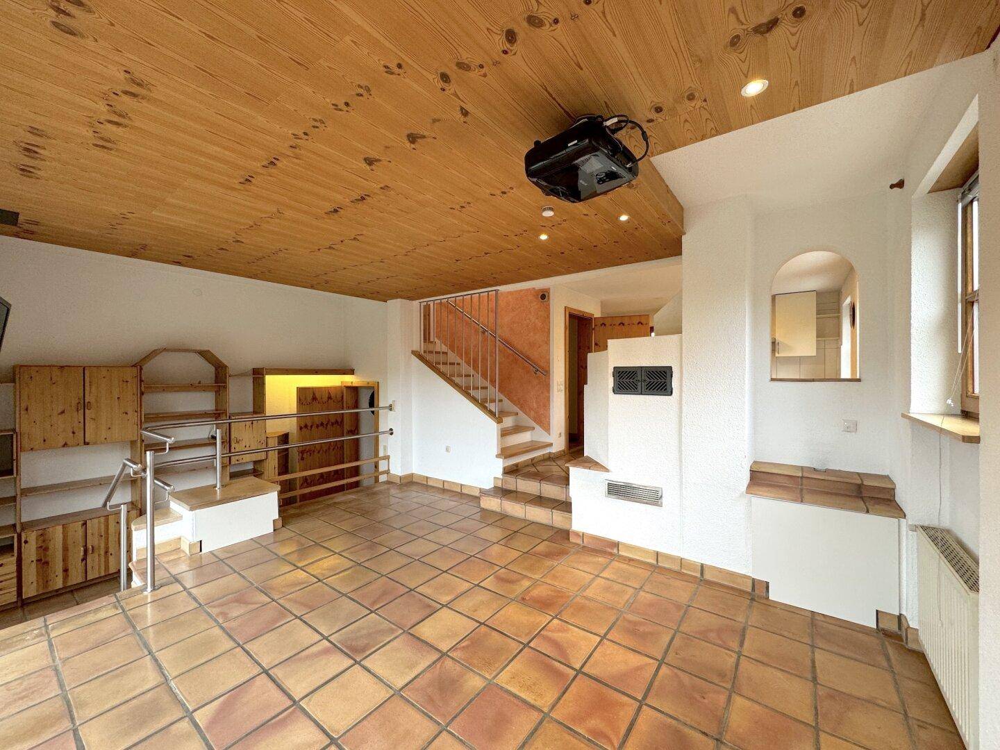 Gemütlicher Wohnbereich mit Kachelofen, Holzdecke und integrierten Holzregalen, ideal für gesellige Abende.