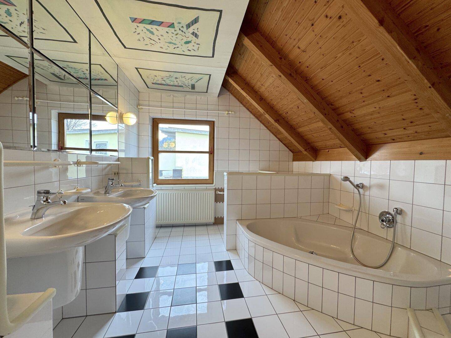 Geräumiges Badezimmer im Dachgeschoss mit Doppelwaschbecken, Eckbadewanne und Holzdachschrägen.