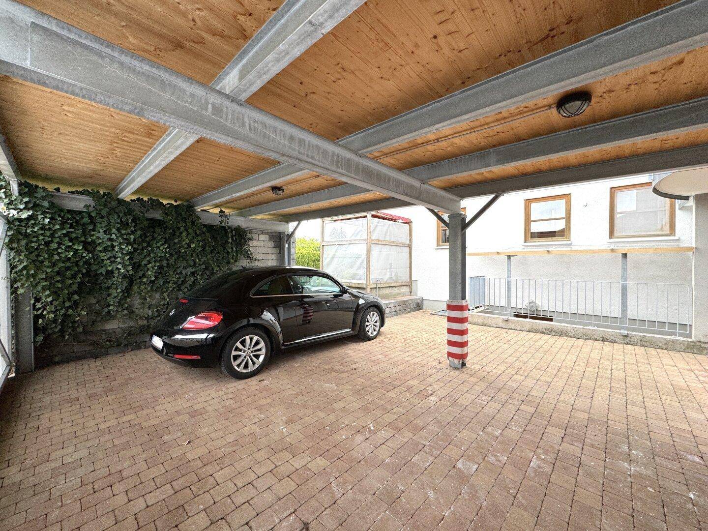 Geräumiger Carport mit Holzdach und Metallkonstruktion, bietet Schutz für Fahrzeuge.