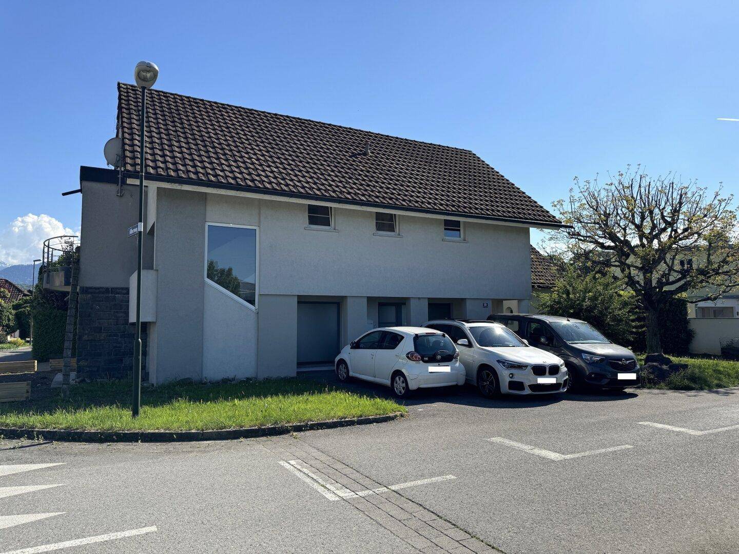 Ansicht des Hauses von der Straße mit geparkten Autos und einem klaren blauen Himmel.