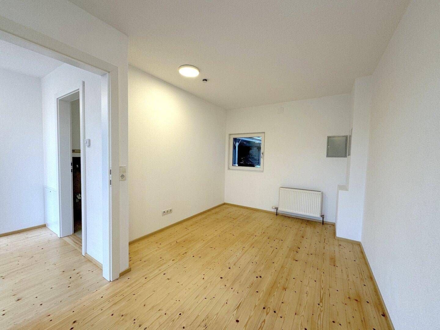 Helles, leeres Zimmer mit Holzboden und weißen Wänden, bereit zur individuellen Gestaltung.