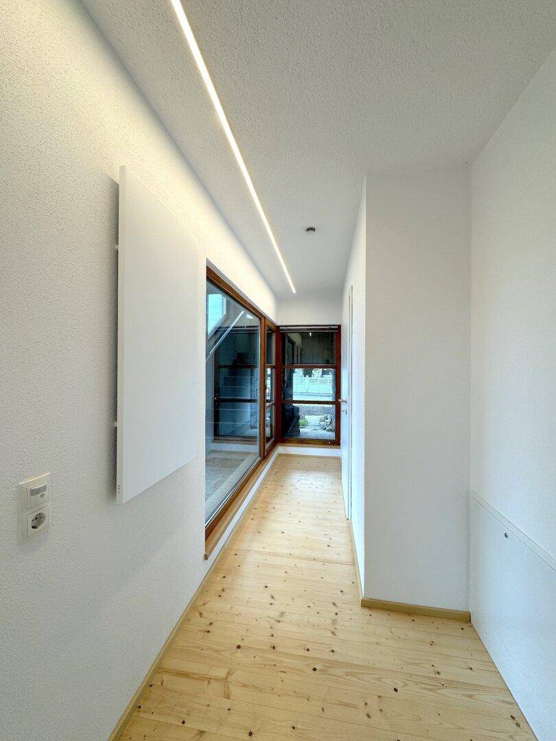 Heller Flur mit Holzboden und langen Fenstern, die viel natürliches Licht hereinlassen.