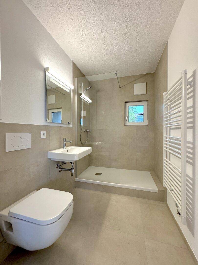 Modernes Badezimmer mit ebenerdiger Dusche, Wand-WC und beheiztem Handtuchhalter.