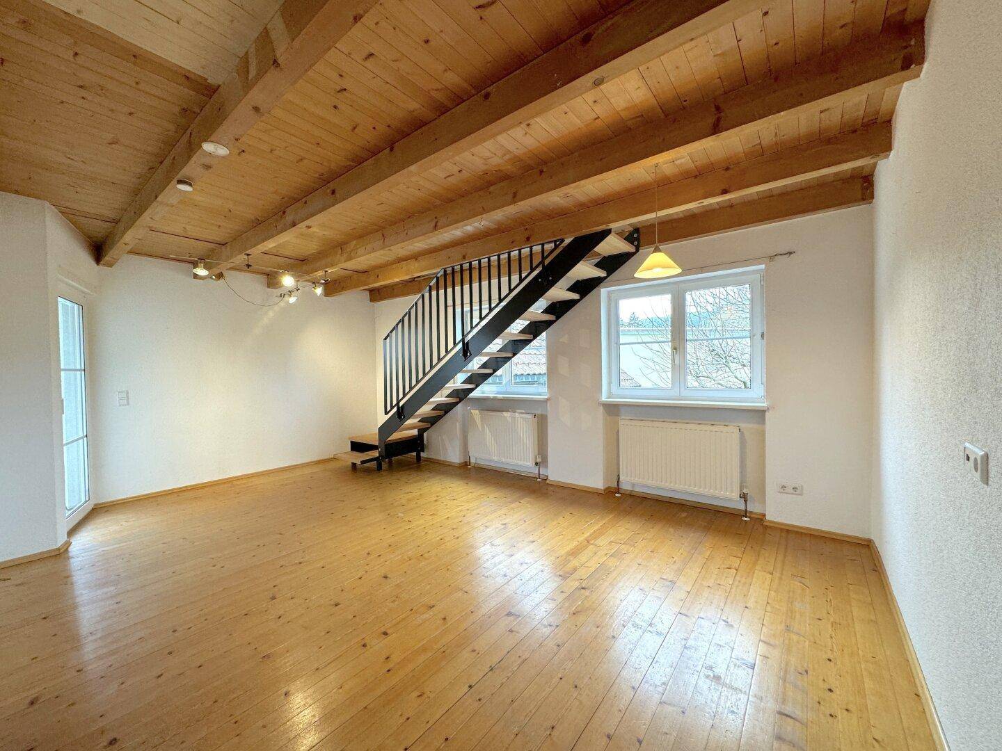 Geräumiges Wohnzimmer mit Holzboden, sichtbaren Deckenbalken und einer modernen Treppe.