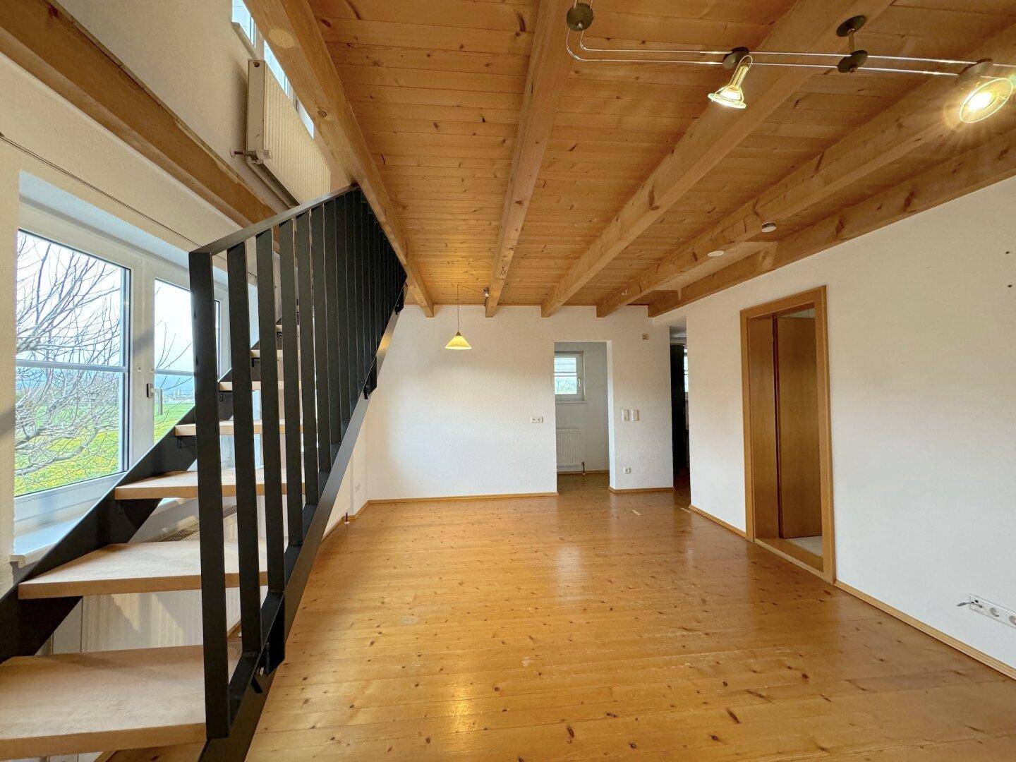 Heller Wohnbereich mit Holzboden, offener Treppe und sichtbaren Deckenbalken, die Charakter verleihen.