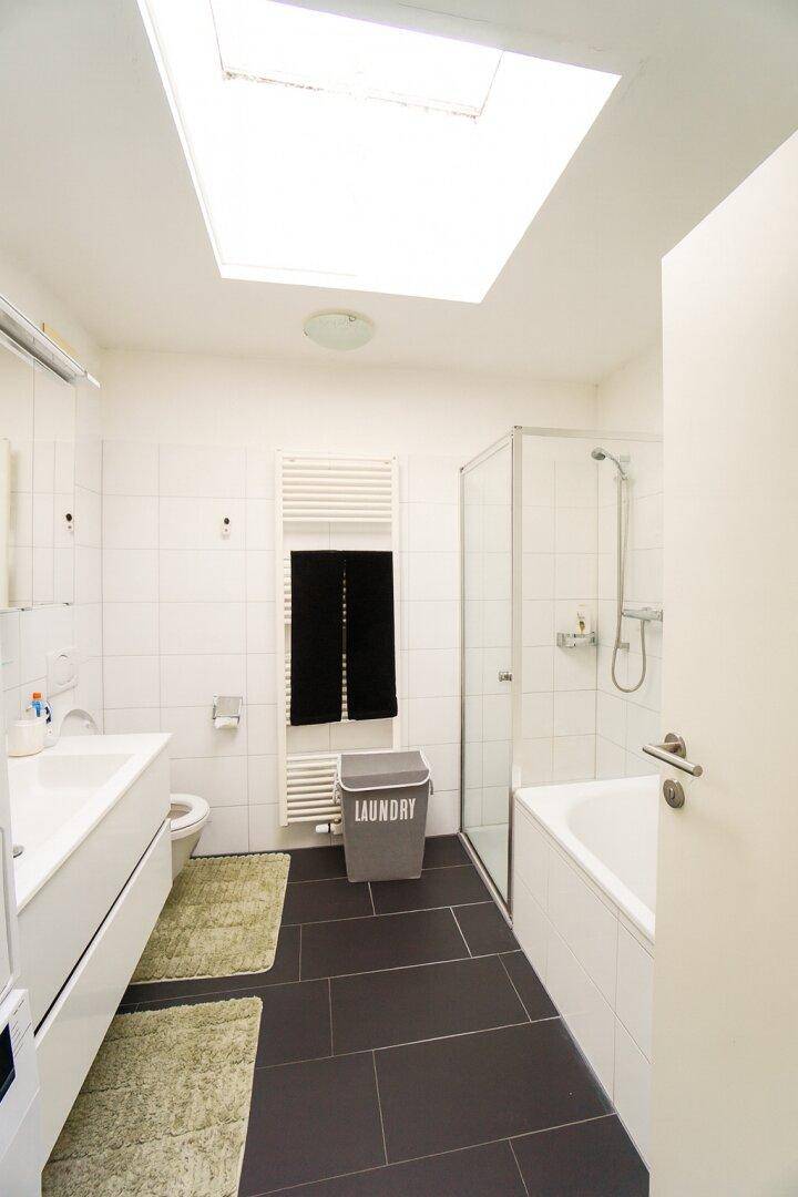 Modernes Badezimmer mit Badewanne, Dusche, Dachfenster und dunklen Bodenfliesen.