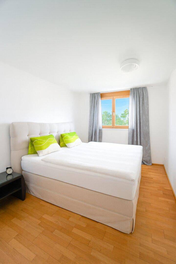 Helles Schlafzimmer mit Doppelbett, Holzparkett und Fenster mit Blick ins Grüne.