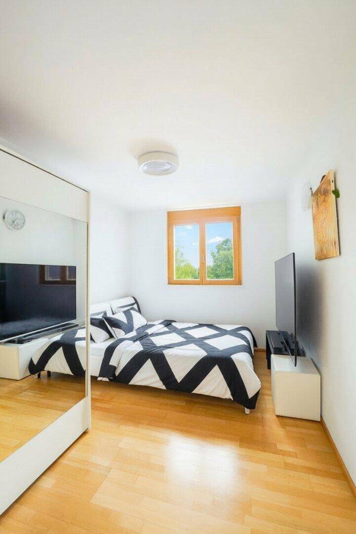 Modern eingerichtetes Schlafzimmer mit Holzparkett, großem Spiegel und Fernseher.