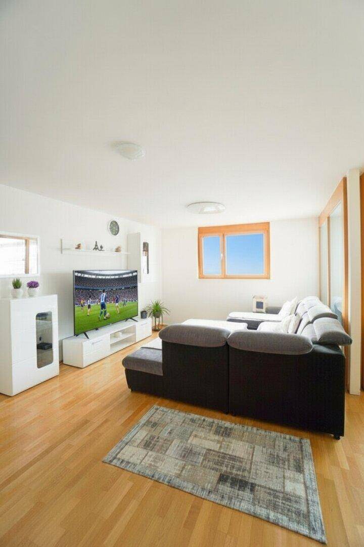 Gemütliches Wohnzimmer mit großem Sofa, Holzparkett und viel Tageslicht.