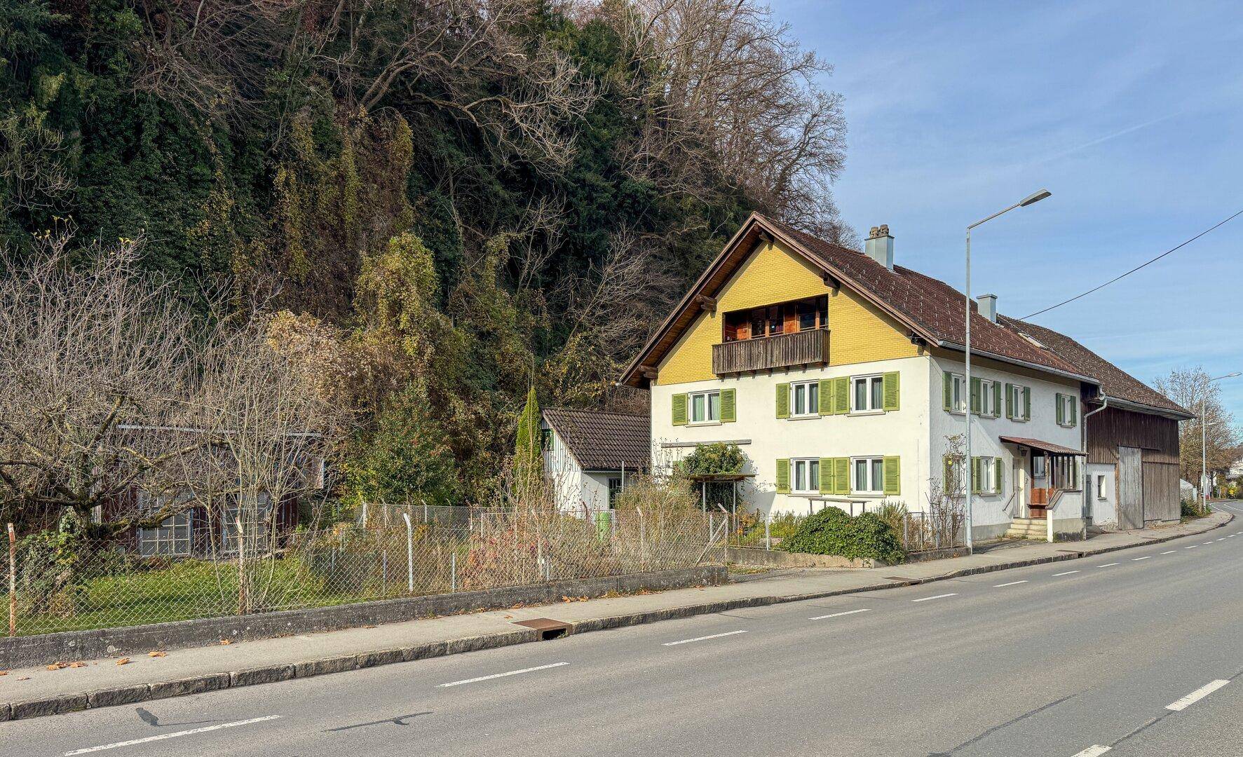Seitenansicht des Wohnhauses mit Balkon und der angrenzenden Scheune an der Straße.