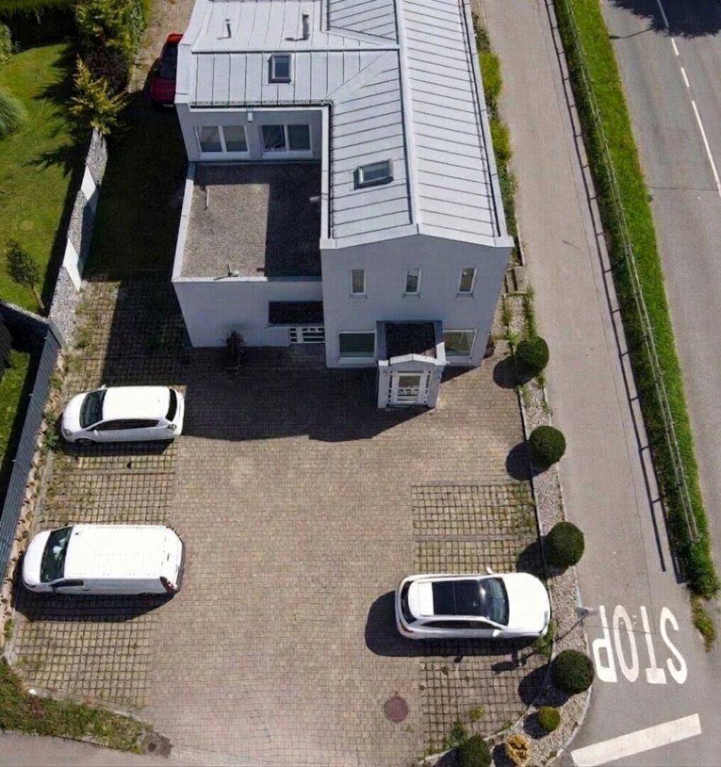 Luftaufnahme des Gebäudes mit detaillierter Dachansicht und gepflastertem Parkplatz mit mehreren Fahrzeugen.